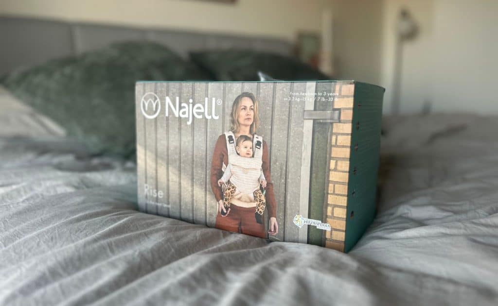 Förpackning innehållande najell rise bärsele på en säng.